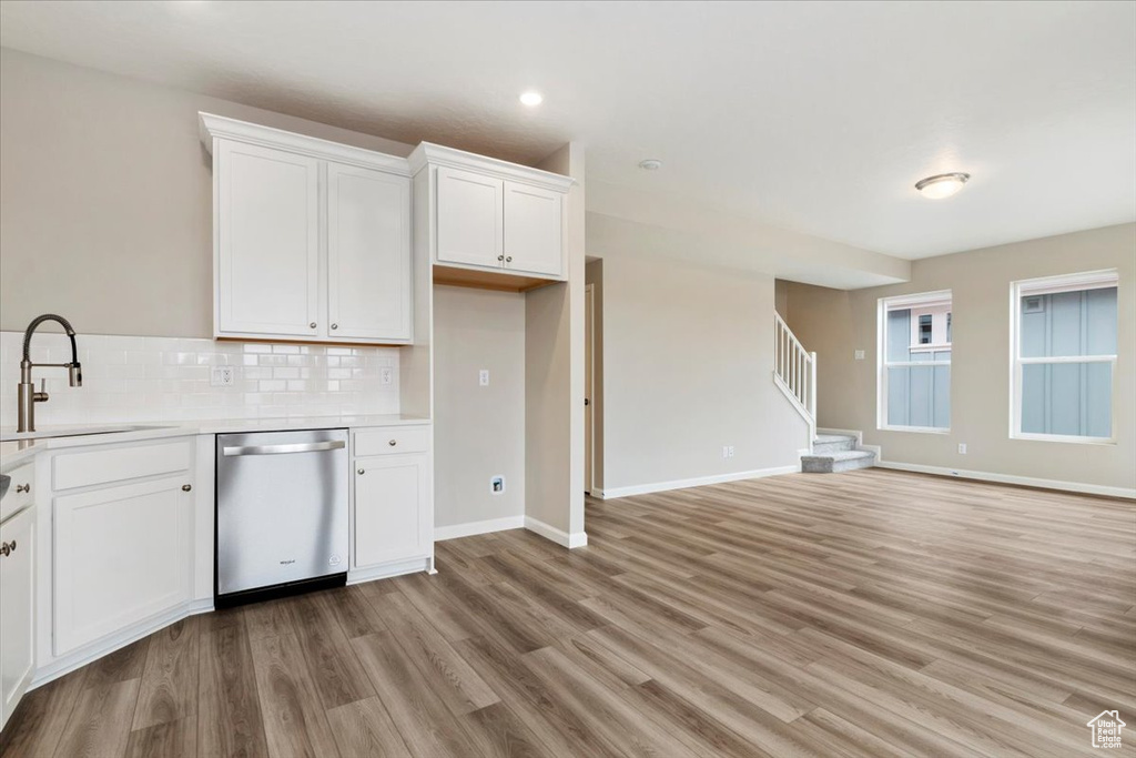 Kitchen featuring light hardwood / wood-style floors, tasteful backsplash, dishwasher, sink, and white cabinets