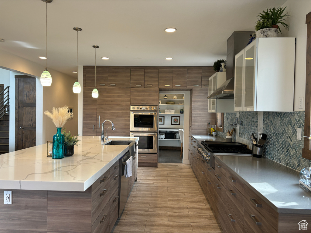 Kitchen with hanging light fixtures, appliances with stainless steel finishes, an island with sink, and tasteful backsplash