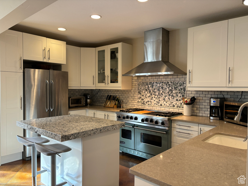 Kitchen with a kitchen breakfast bar, tasteful backsplash, white cabinetry, wall chimney exhaust hood, and appliances with stainless steel finishes