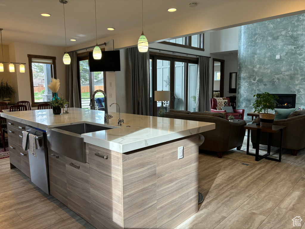 Kitchen featuring light stone counters, a fireplace, a spacious island, dishwasher, and pendant lighting