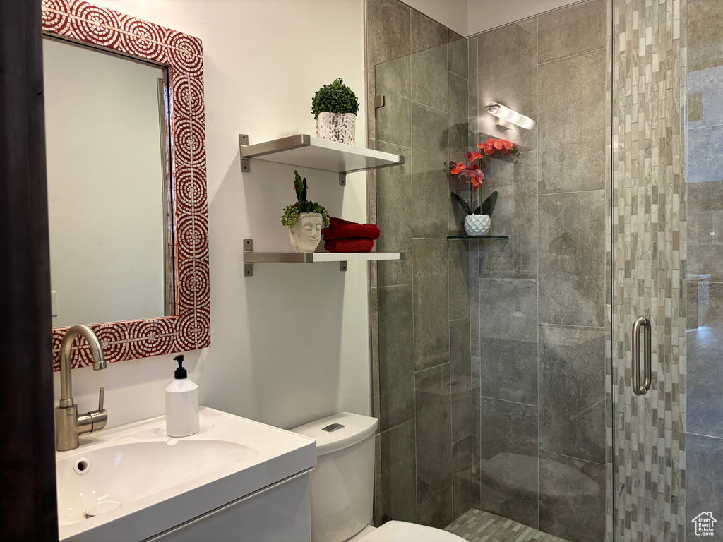 Bathroom featuring a shower with shower door, vanity, and toilet