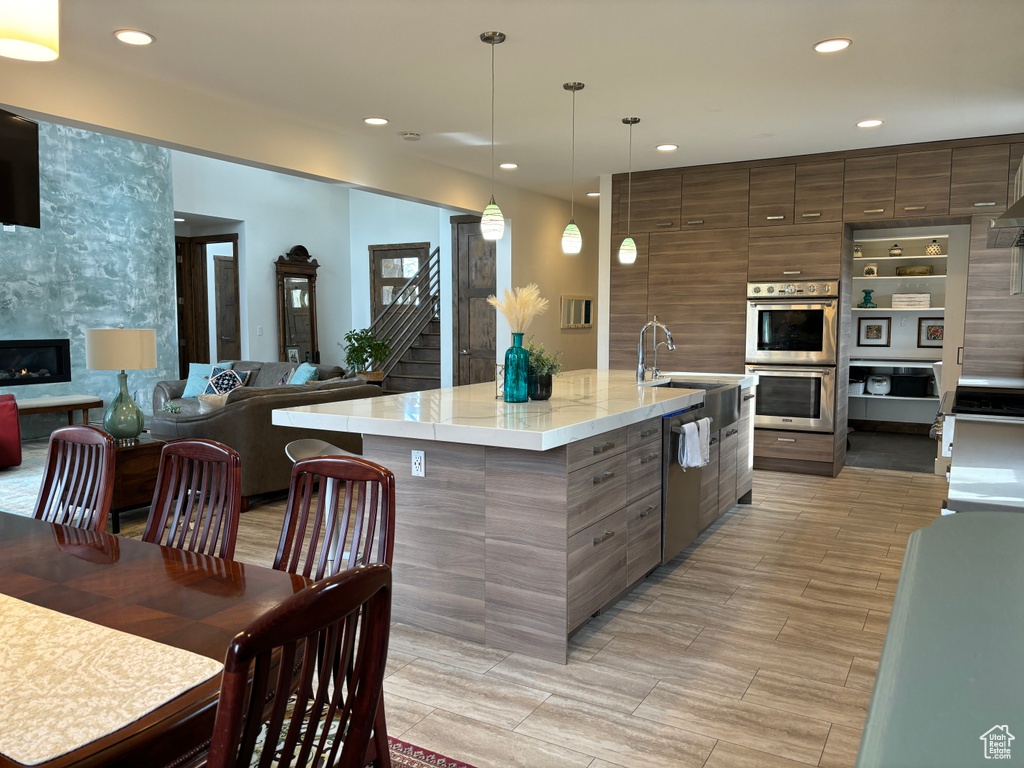 Kitchen with hanging light fixtures, a fireplace, stainless steel appliances, an island with sink, and sink