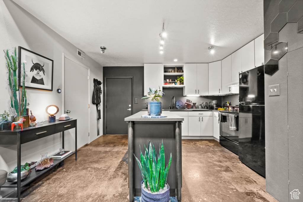 Kitchen with a kitchen island, black fridge, range with electric cooktop, track lighting, and white cabinets