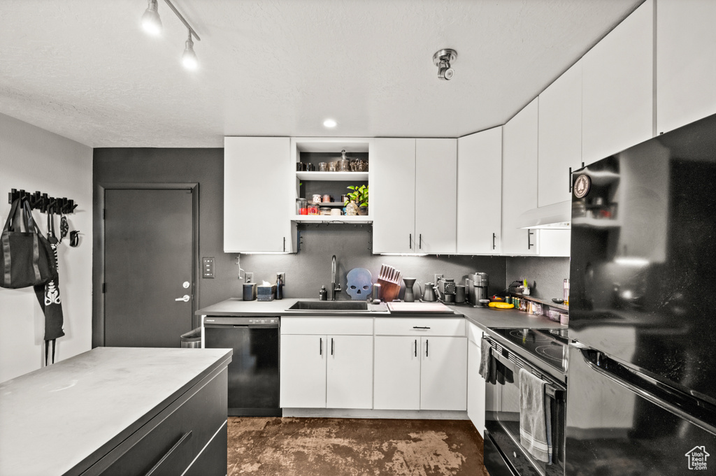 Kitchen featuring black appliances, track lighting, wall chimney range hood, sink, and white cabinetry