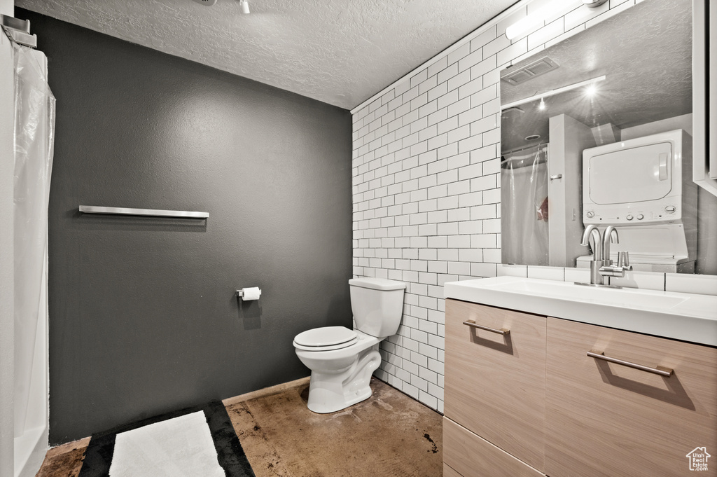 Bathroom with tile walls, stacked washer and dryer, toilet, vanity, and a textured ceiling