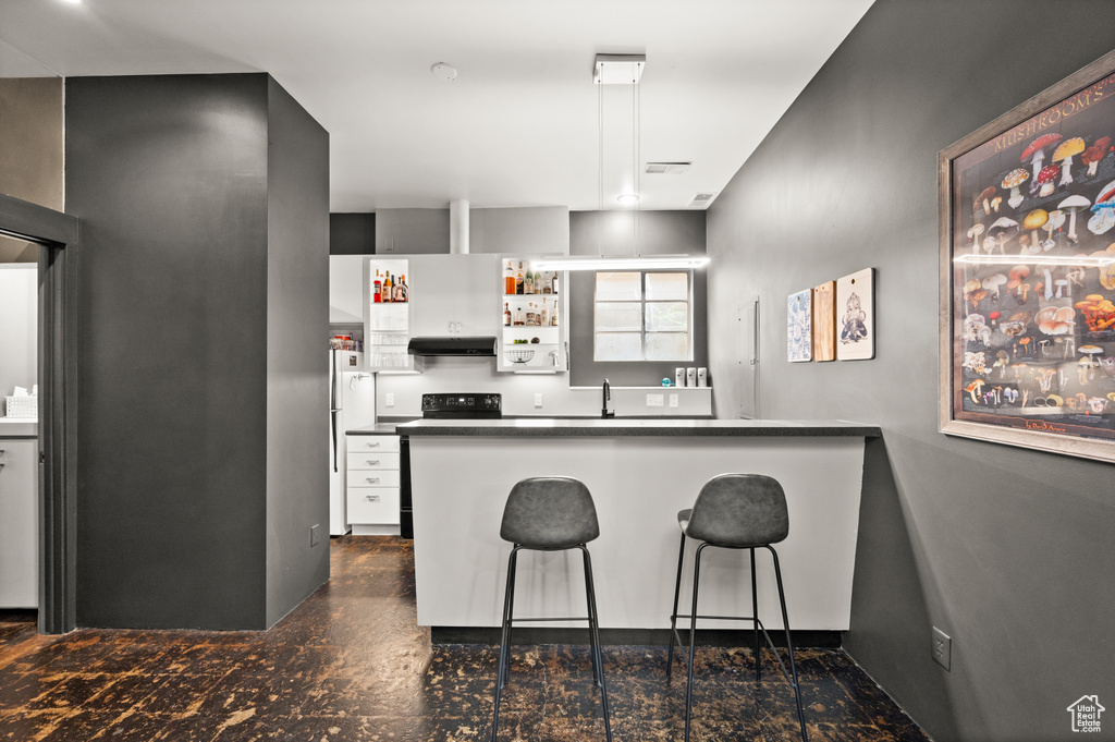 Kitchen with white cabinetry, black range with electric stovetop, kitchen peninsula, and a kitchen bar