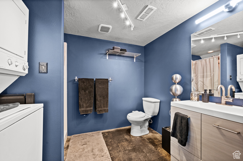 Bathroom featuring stacked washer / dryer, a textured ceiling, rail lighting, toilet, and vanity