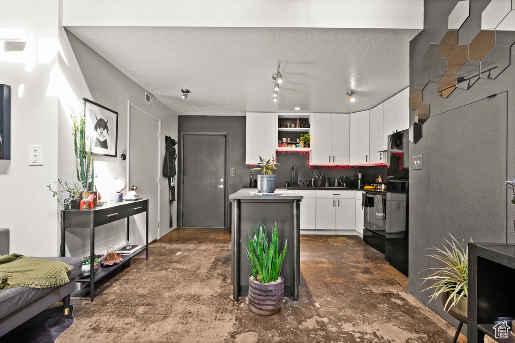 Kitchen with stainless steel range with electric cooktop, a textured ceiling, track lighting, backsplash, and white cabinets