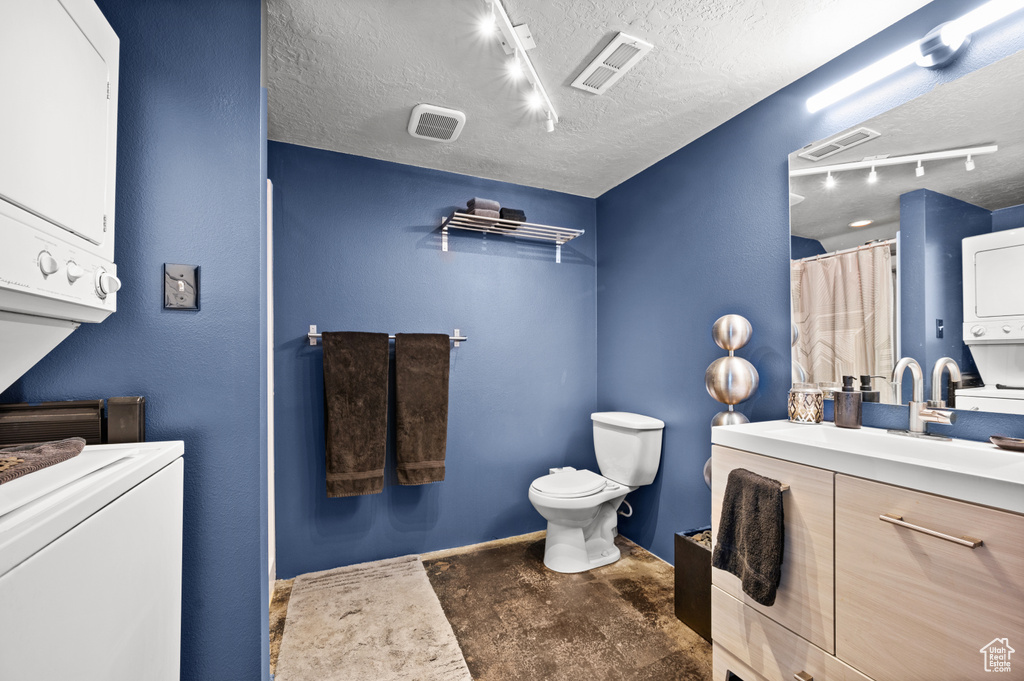 Bathroom featuring toilet, stacked washer and dryer, rail lighting, vanity, and a textured ceiling