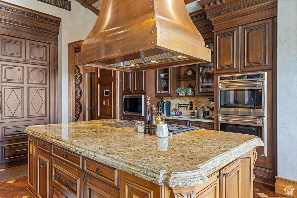 Kitchen featuring a center island, appliances with stainless steel finishes, premium range hood, light stone counters, and tasteful backsplash