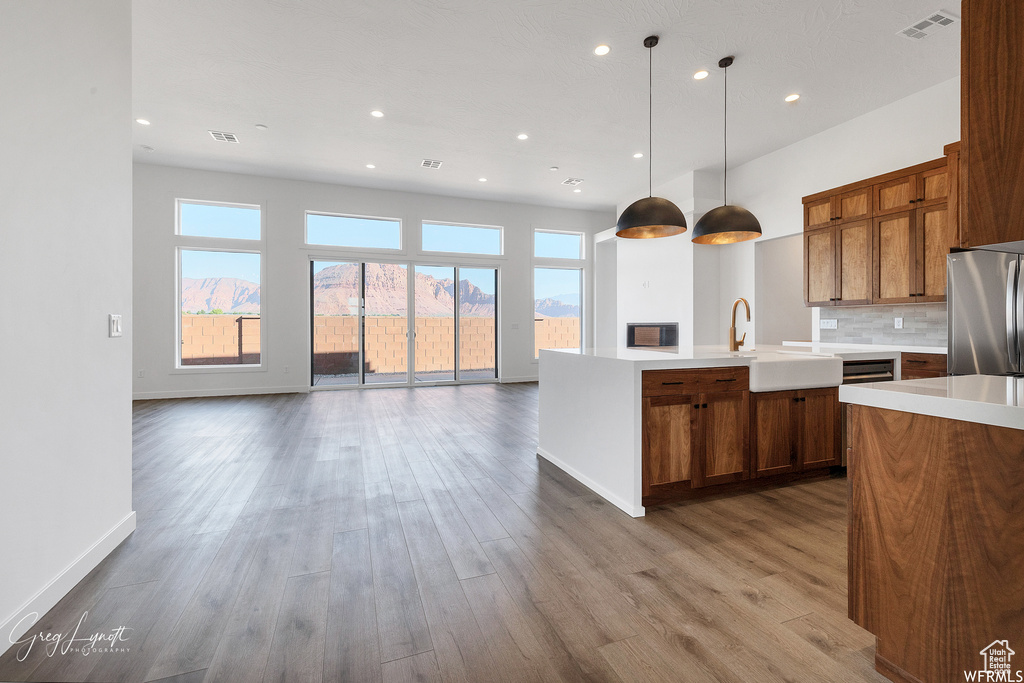 Kitchen with stainless steel refrigerator, backsplash, hanging light fixtures, wood-type flooring, and sink