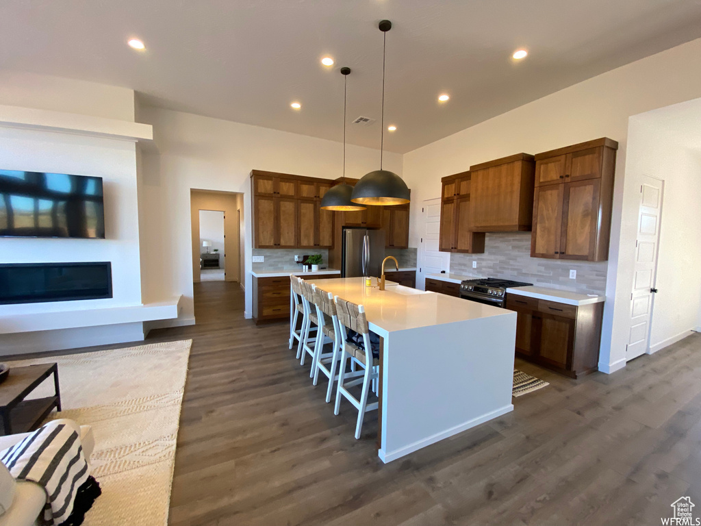 Kitchen with dark hardwood / wood-style floors, decorative light fixtures, backsplash, a kitchen island with sink, and appliances with stainless steel finishes