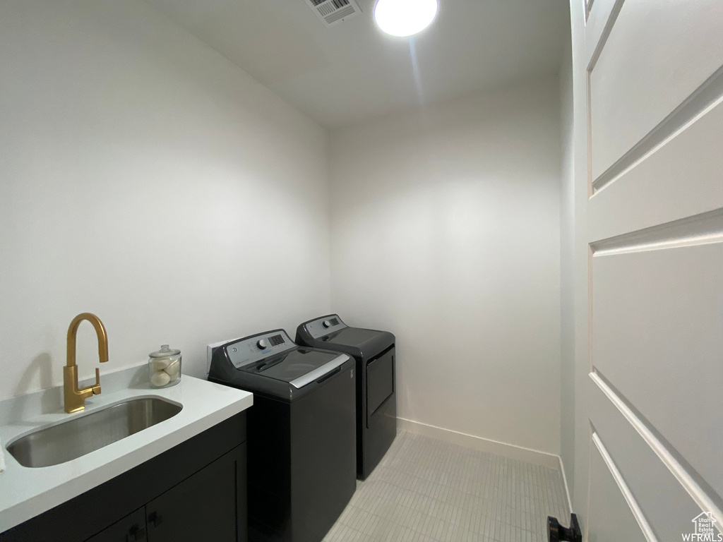 Clothes washing area featuring separate washer and dryer, sink, and light tile flooring