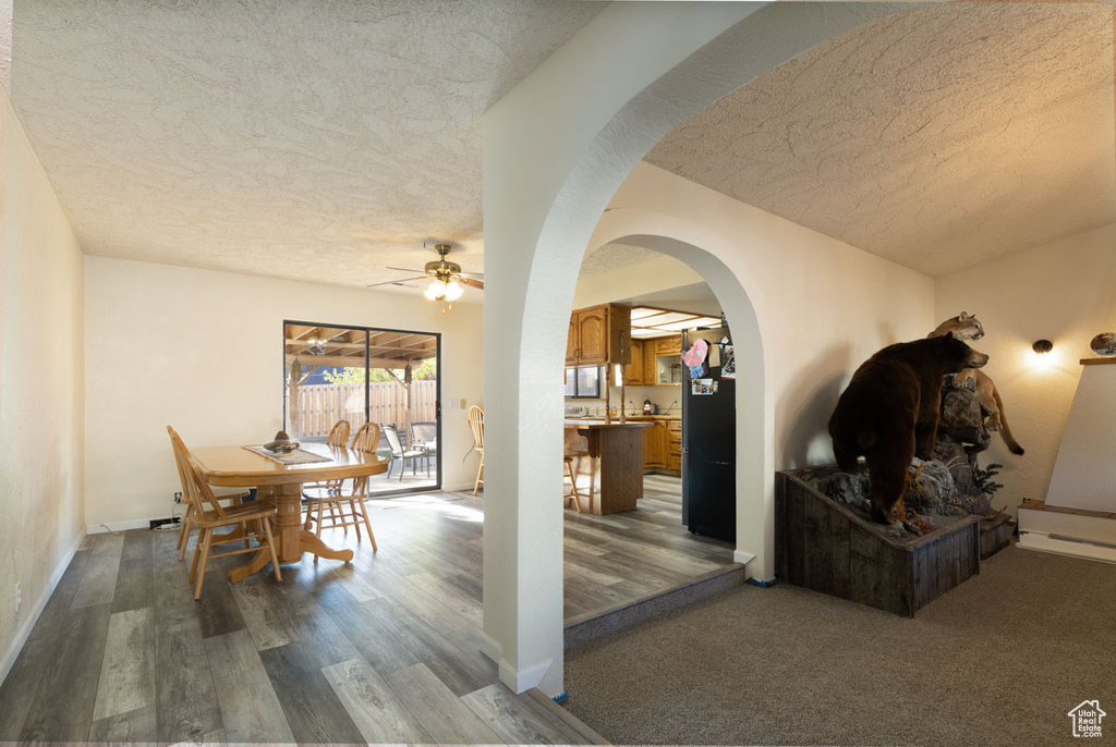 Dining room featuring a textured ceiling, baseboard heating, dark colored carpet, and ceiling fan