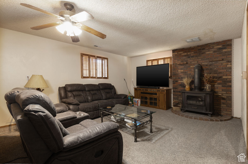 Carpeted living room with ceiling fan, a textured ceiling, and a wood stove