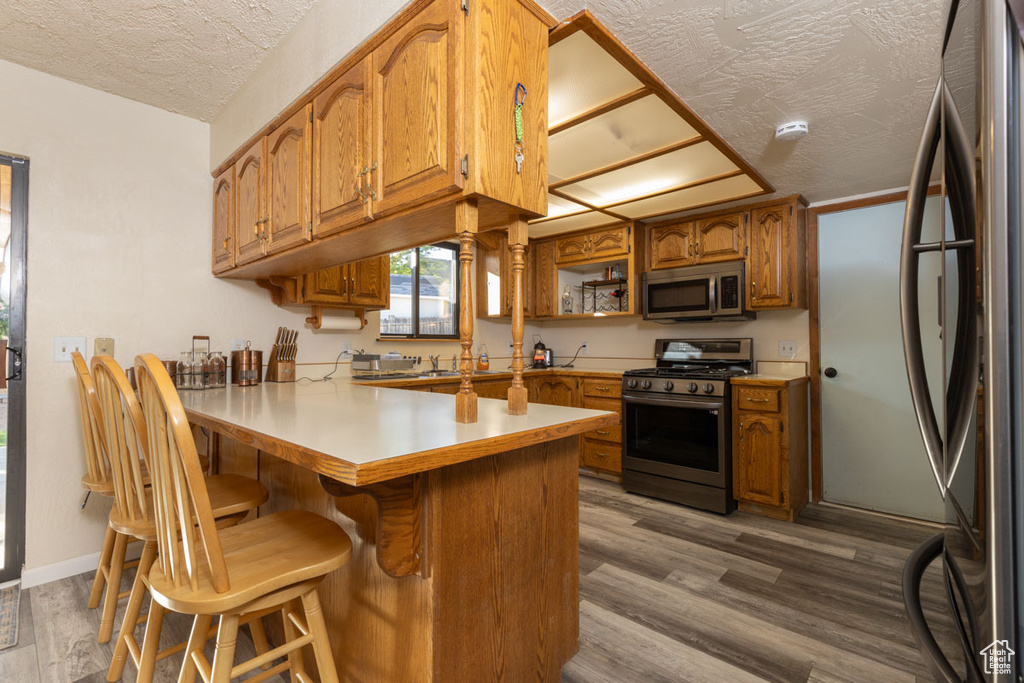Kitchen featuring a textured ceiling, hardwood / wood-style floors, kitchen peninsula, and stainless steel appliances