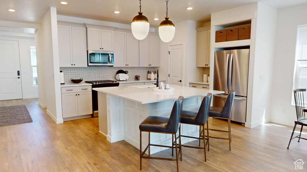 Kitchen featuring stainless steel appliances, an island with sink, light hardwood / wood-style flooring, and tasteful backsplash