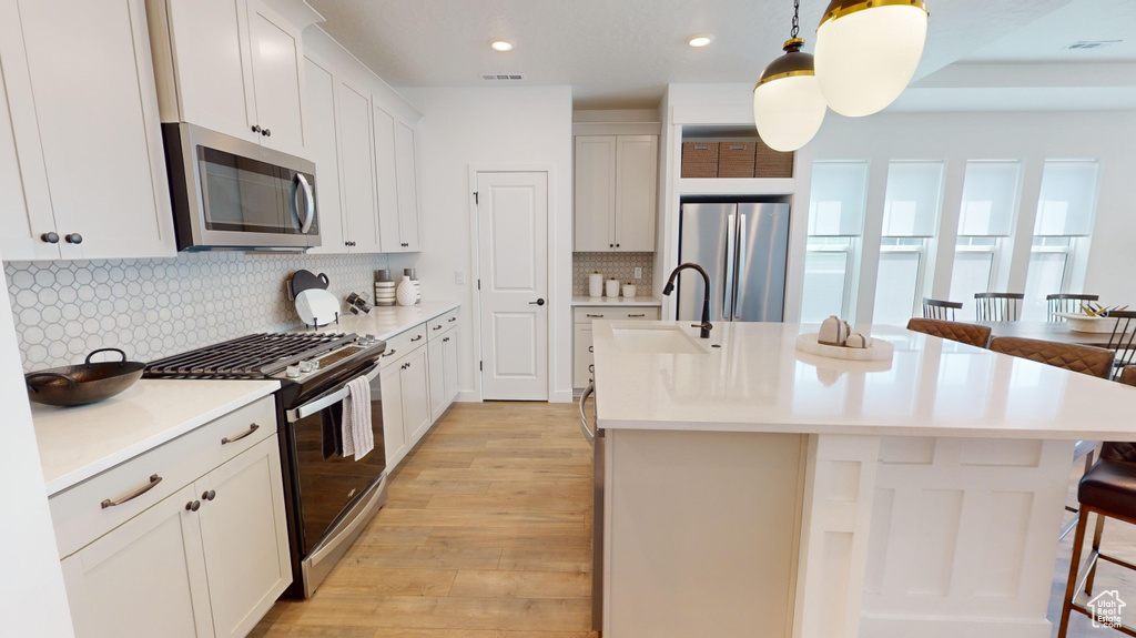 Kitchen with stainless steel appliances, an island with sink, decorative light fixtures, backsplash, and sink