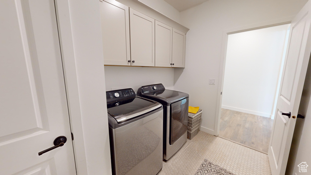 Clothes washing area with cabinets, light wood-type flooring, and independent washer and dryer