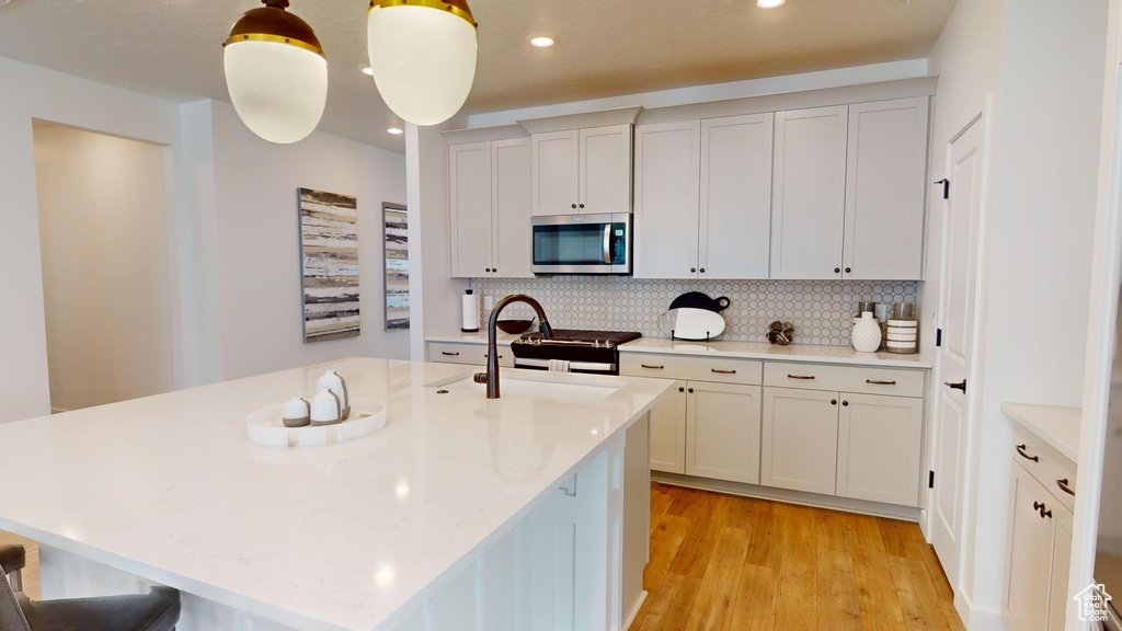 Kitchen featuring decorative light fixtures, a center island with sink, tasteful backsplash, light wood-type flooring, and white cabinets