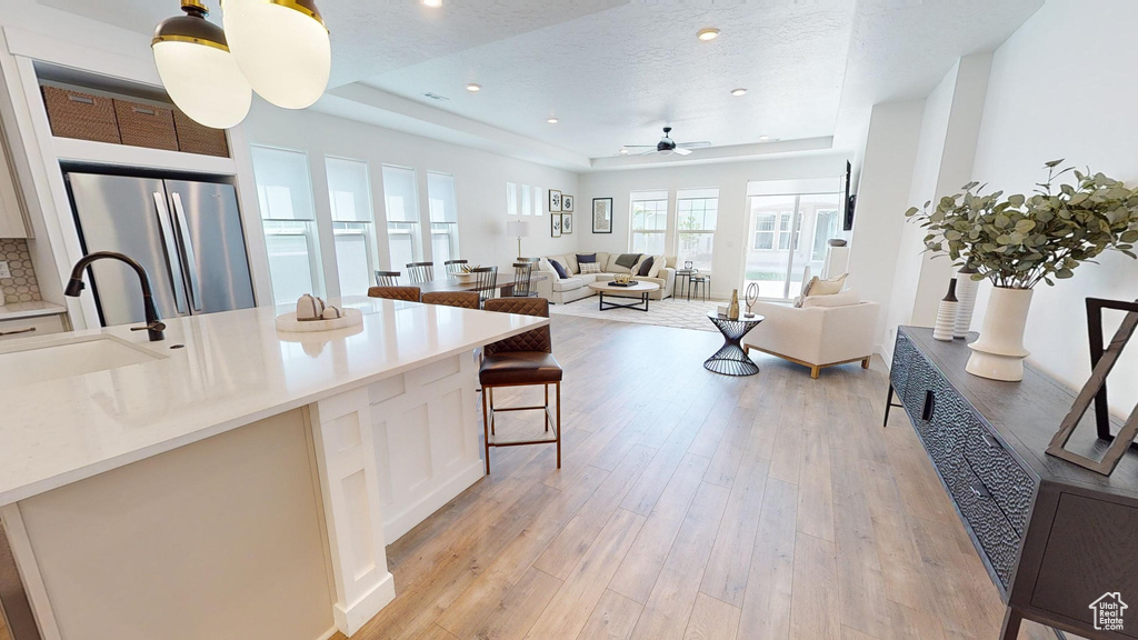 Kitchen with light wood-type flooring, a tray ceiling, stainless steel refrigerator, sink, and ceiling fan