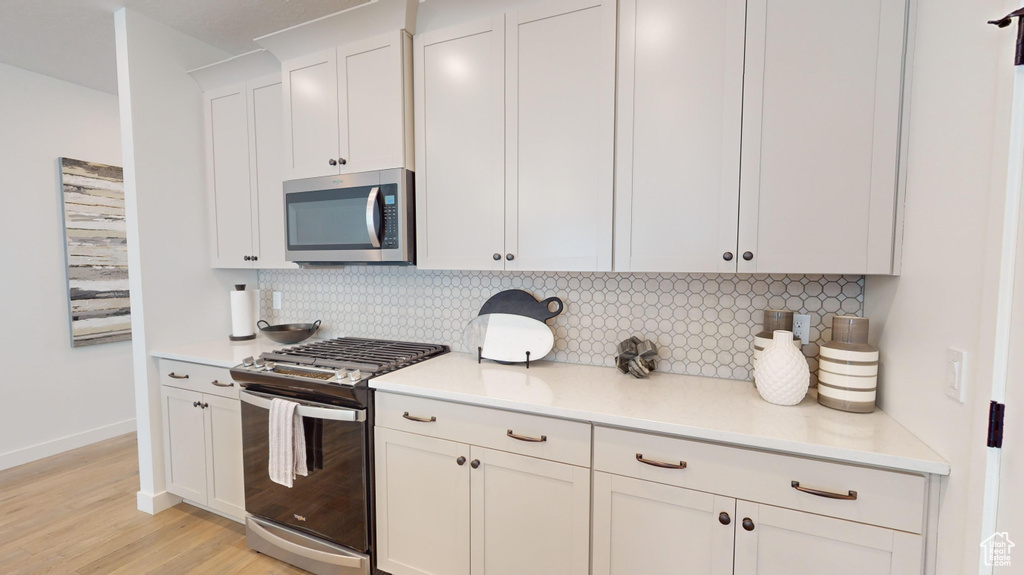 Kitchen with stainless steel appliances, white cabinetry, light hardwood / wood-style flooring, and backsplash