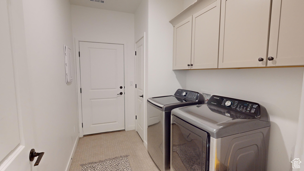 Clothes washing area with cabinets, light tile floors, and washing machine and dryer