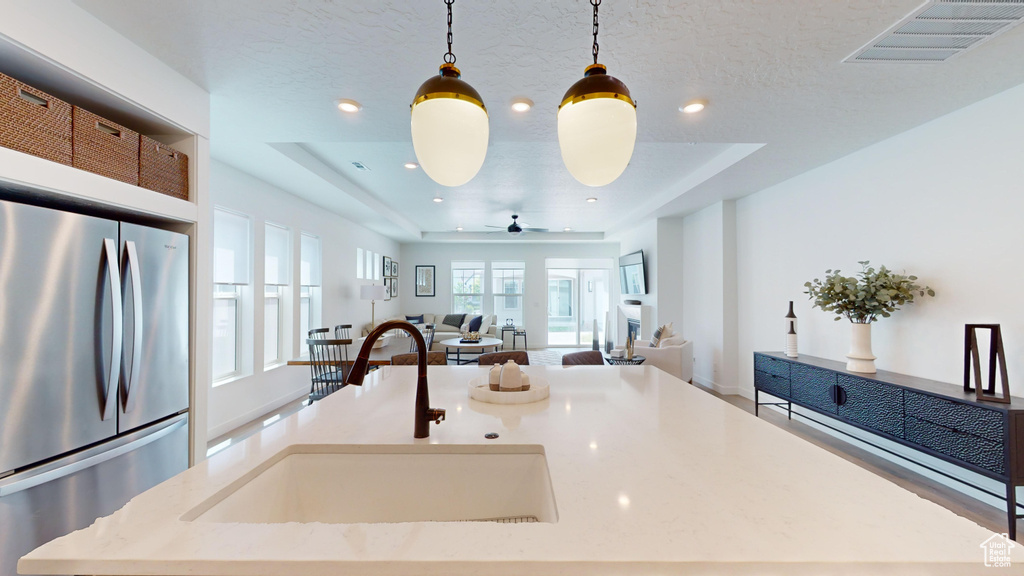 Kitchen featuring a center island, decorative light fixtures, stainless steel refrigerator, sink, and a raised ceiling