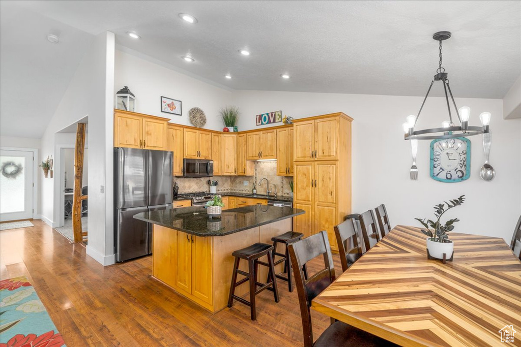 Kitchen featuring a kitchen island, stainless steel appliances, hardwood / wood-style floors, decorative light fixtures, and tasteful backsplash