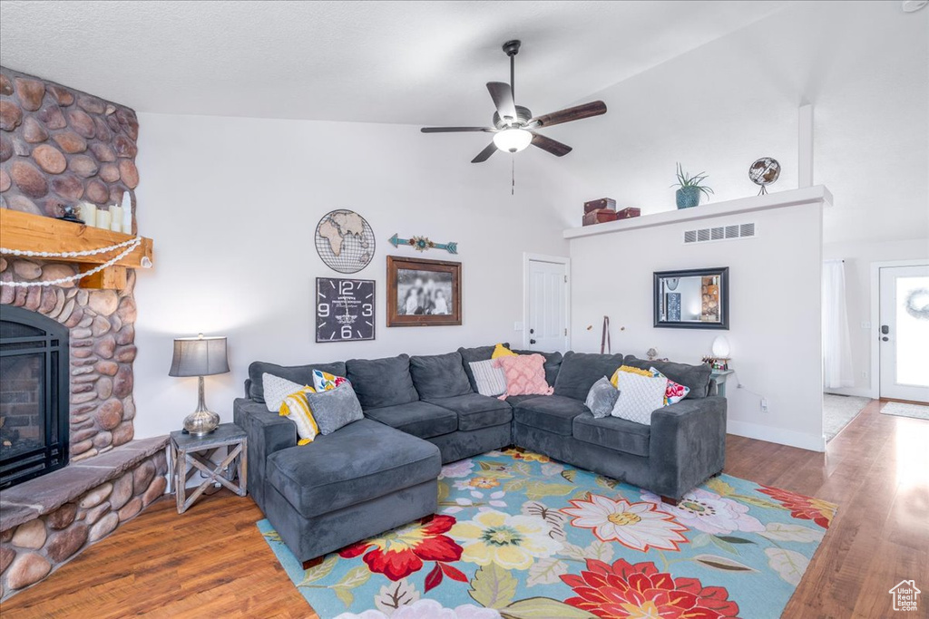 Living room with high vaulted ceiling, wood-type flooring, a stone fireplace, and ceiling fan