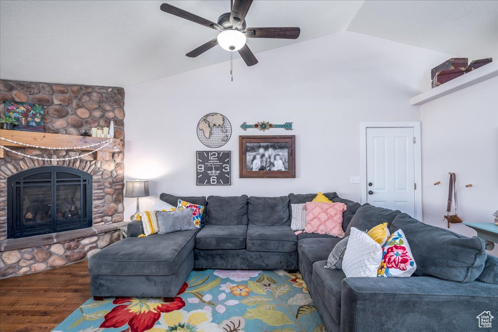 Living room with dark wood-type flooring, a stone fireplace, ceiling fan, and lofted ceiling