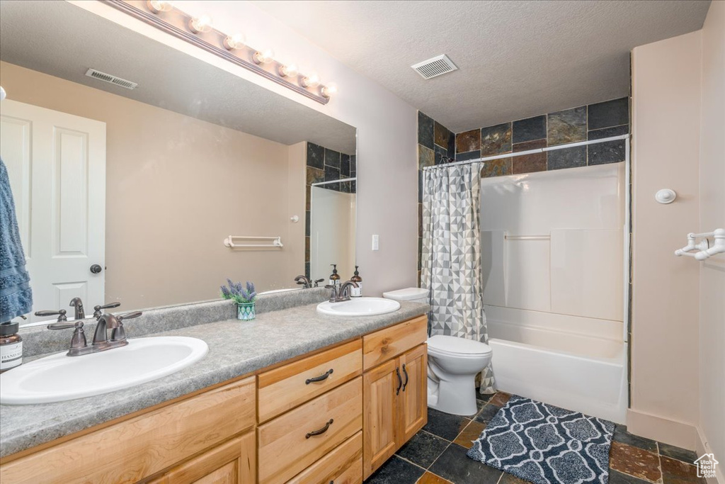 Full bathroom featuring shower / bath combo with shower curtain, tile floors, oversized vanity, toilet, and dual sinks