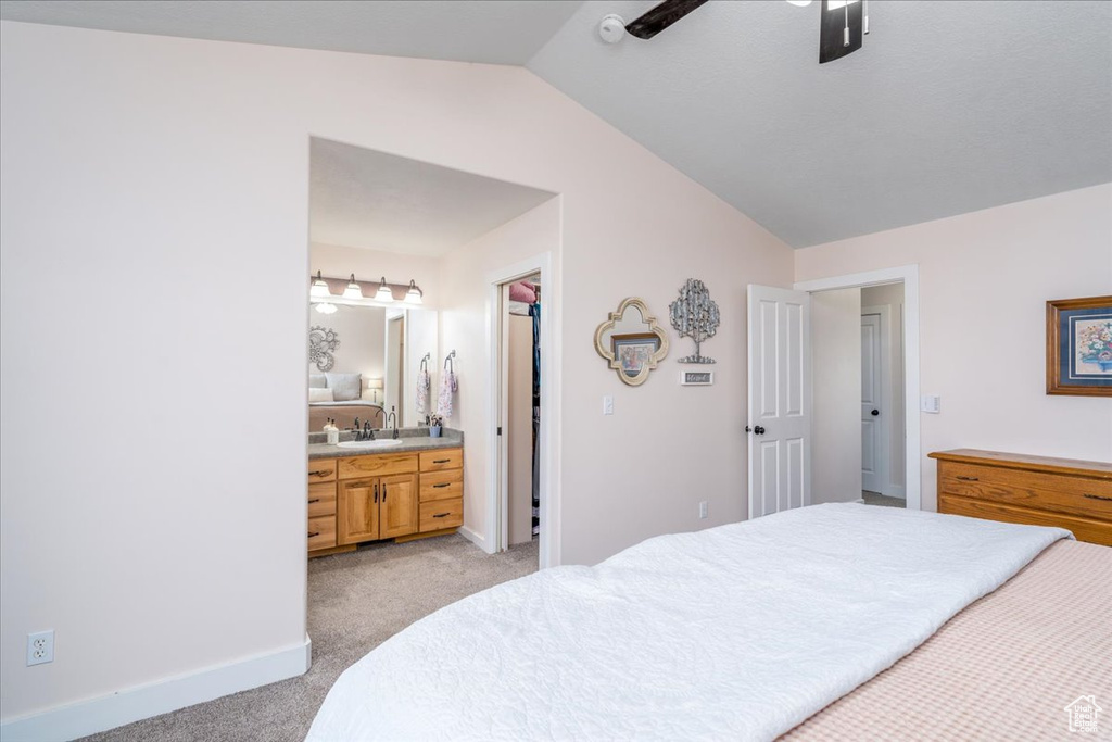 Bedroom featuring ceiling fan, light carpet, vaulted ceiling, ensuite bath, and a walk in closet