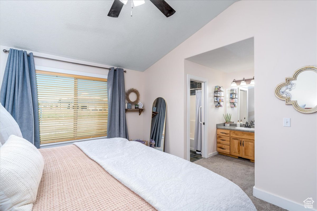 Carpeted bedroom featuring ceiling fan, a walk in closet, sink, connected bathroom, and lofted ceiling