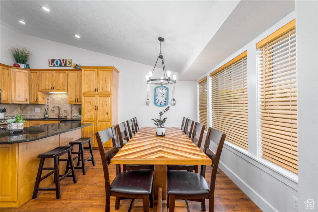 Dining area with sink, lofted ceiling, a chandelier, and wood-type flooring