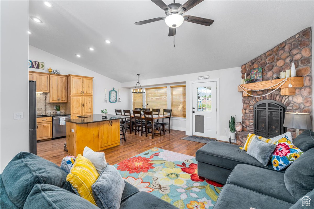 Living room featuring vaulted ceiling, a stone fireplace, ceiling fan, and light wood-type flooring