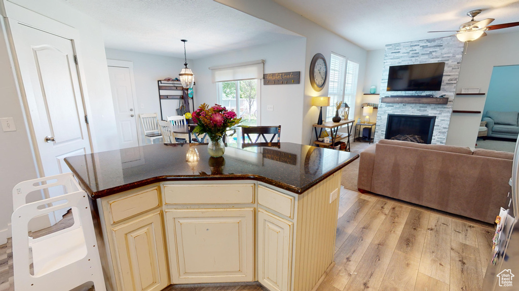 Kitchen with ceiling fan, a stone fireplace, light hardwood / wood-style floors, and a kitchen island