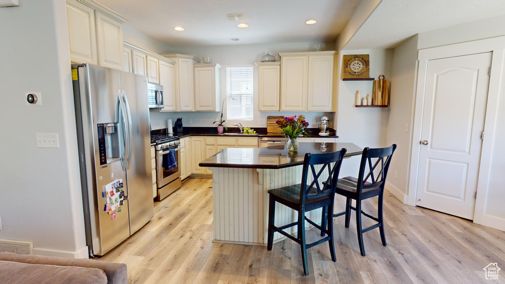 Kitchen featuring light hardwood / wood-style floors, a kitchen island, a breakfast bar area, appliances with stainless steel finishes, and sink