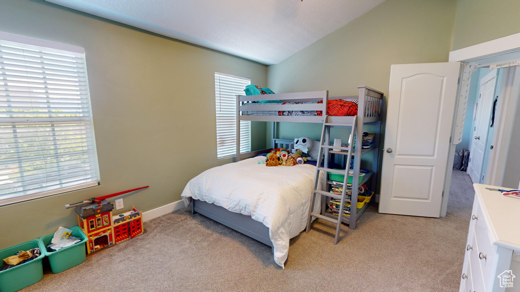 Carpeted bedroom featuring vaulted ceiling and multiple windows