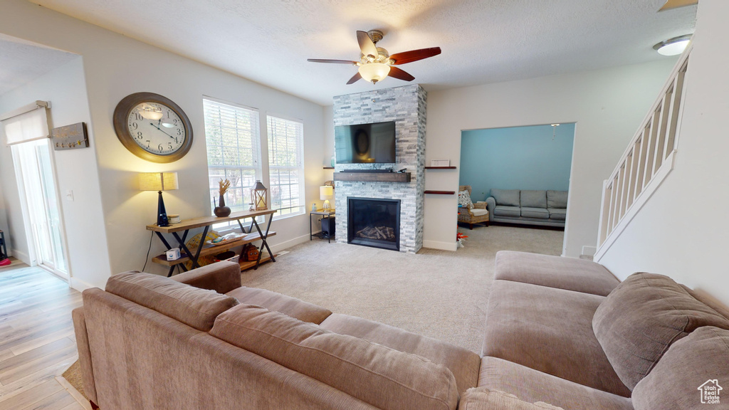 Living room featuring light colored carpet, a stone fireplace, ceiling fan, and a textured ceiling