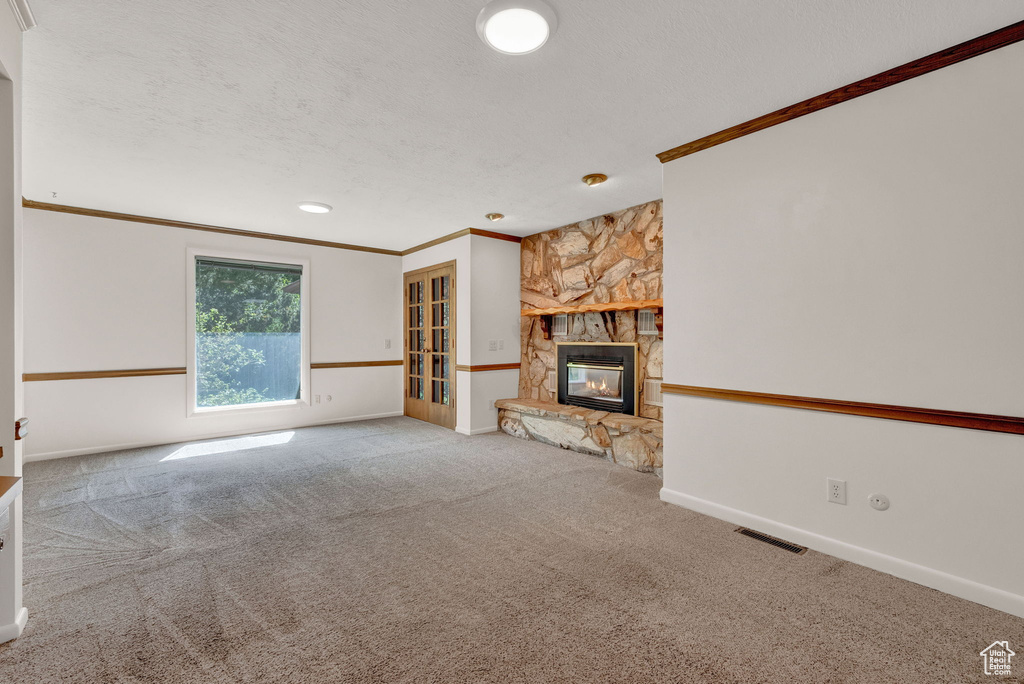 Unfurnished living room with carpet, a stone fireplace, ornamental molding, and a textured ceiling