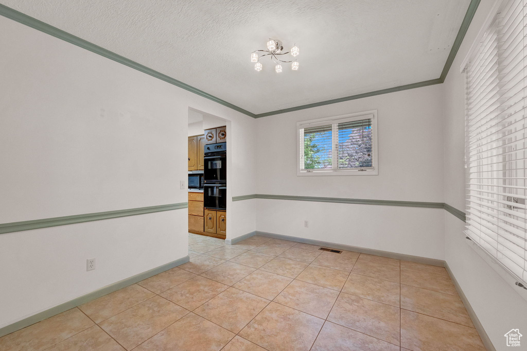 Tiled spare room with a textured ceiling, an inviting chandelier, and crown molding