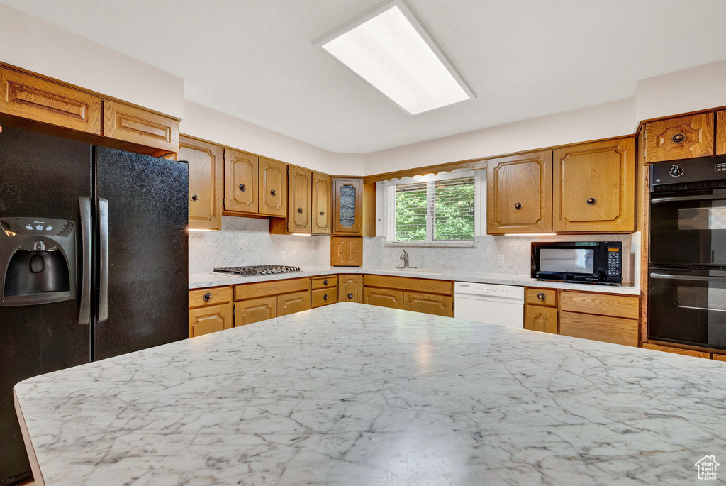 Kitchen with sink, light stone counters, backsplash, and black appliances