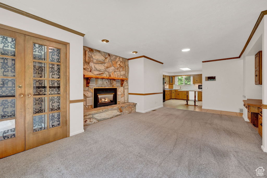 Unfurnished living room with a stone fireplace, ornamental molding, and carpet floors