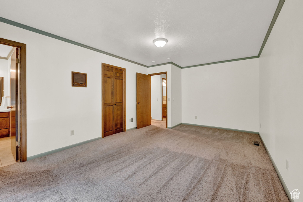 Unfurnished bedroom with light colored carpet, connected bathroom, and ornamental molding