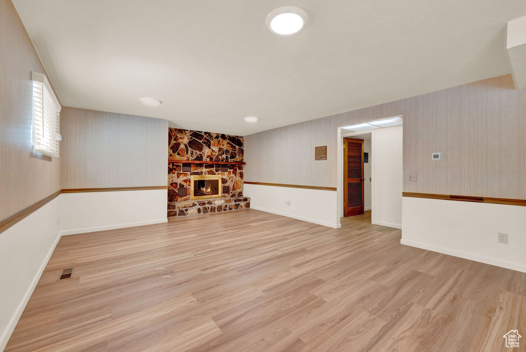 Unfurnished living room featuring a stone fireplace and light hardwood / wood-style floors