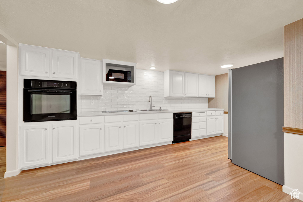 Kitchen featuring sink, black appliances, white cabinets, and light hardwood / wood-style floors