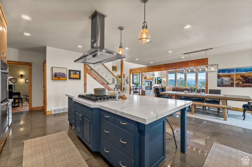 Kitchen featuring island exhaust hood, stainless steel gas stovetop, pendant lighting, blue cabinets, and a center island