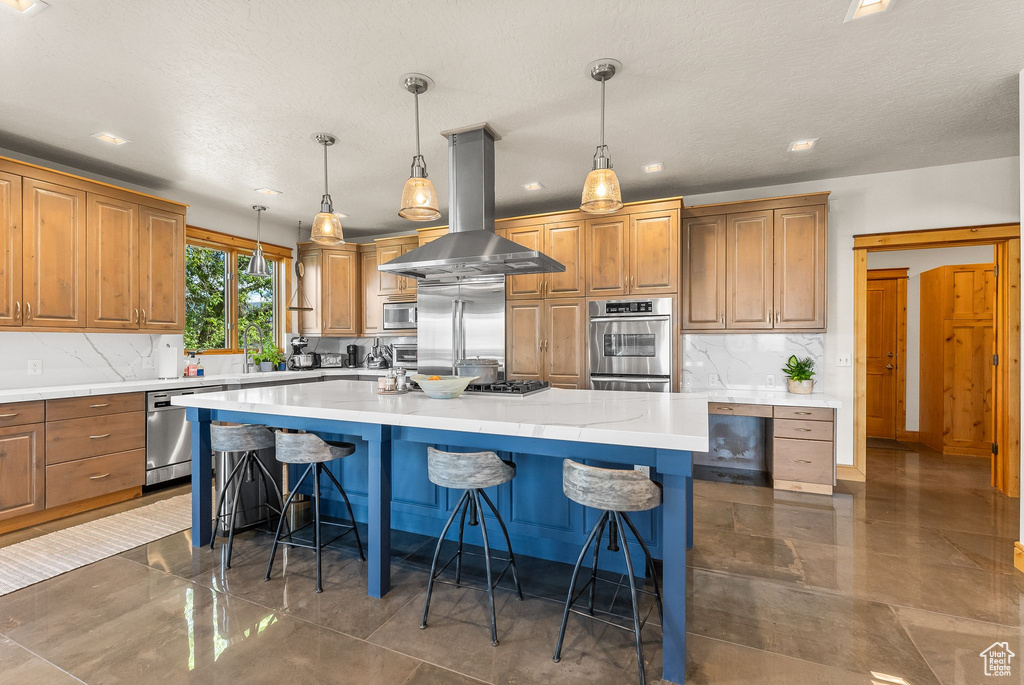 Kitchen with island exhaust hood, tasteful backsplash, built in appliances, pendant lighting, and a large island with sink