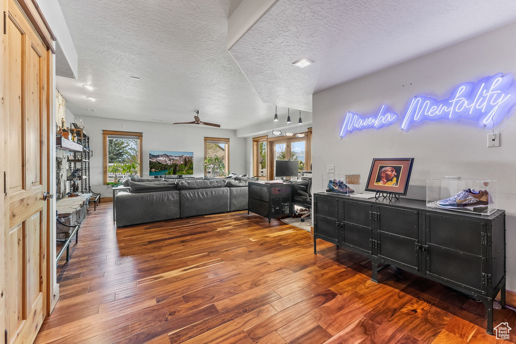 Living room with ceiling fan, a textured ceiling, and dark wood-type flooring